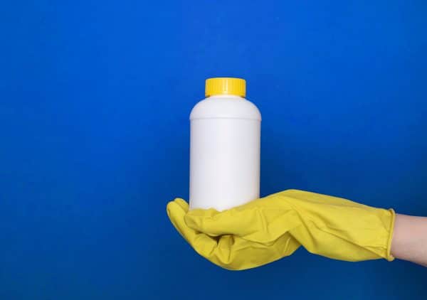 handing holding a bleach bottle in front of a blue background