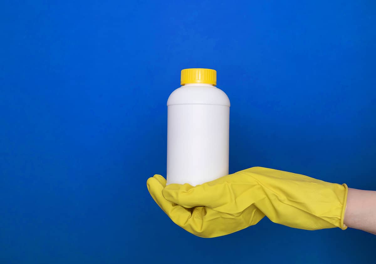 handing holding a bleach bottle in front of a blue background