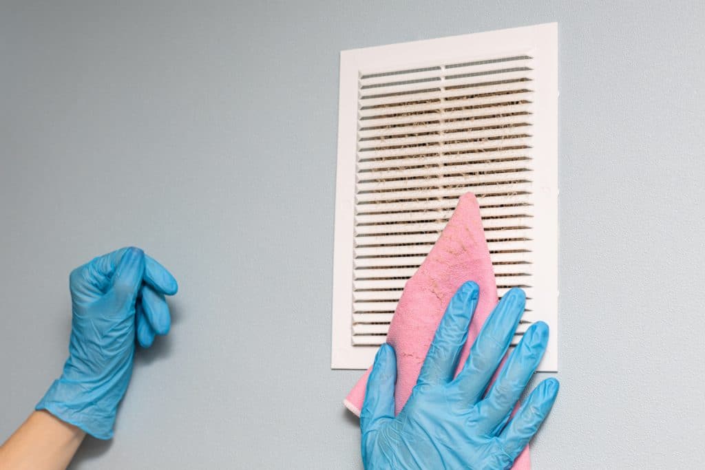 person wearing blue latex gloves cleaning a dirty air vent with a microfiber towel