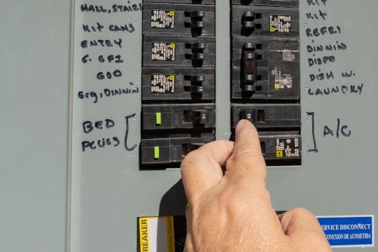 Mans hand resetting tripped ac circuit breaker in an electrical panel