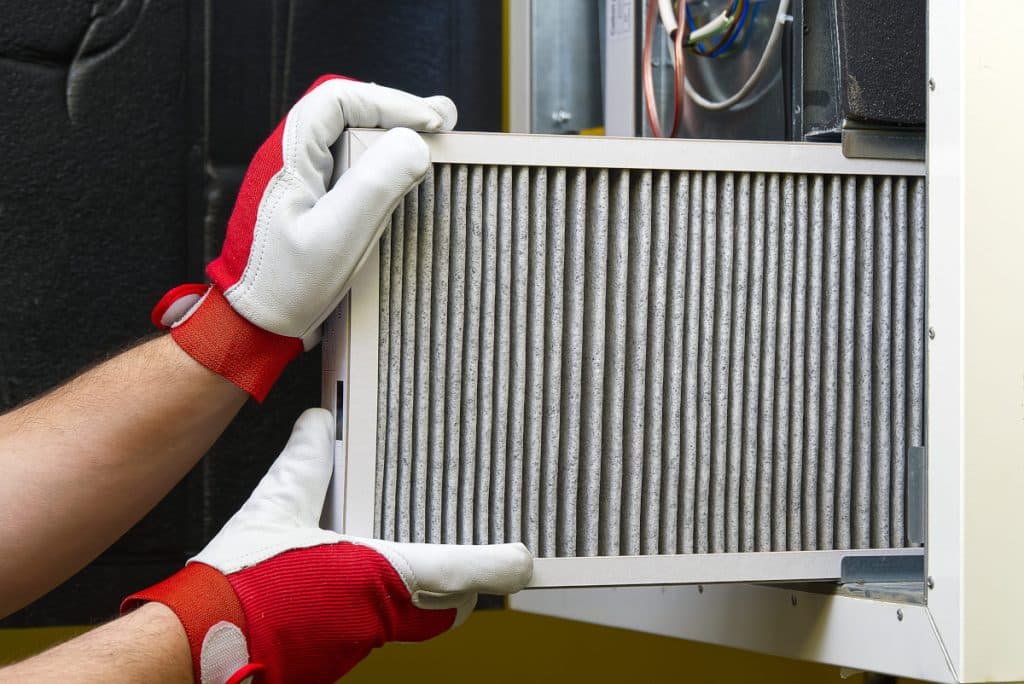 hvac technician with white and red gloves pulling out a dirty hvac air filter